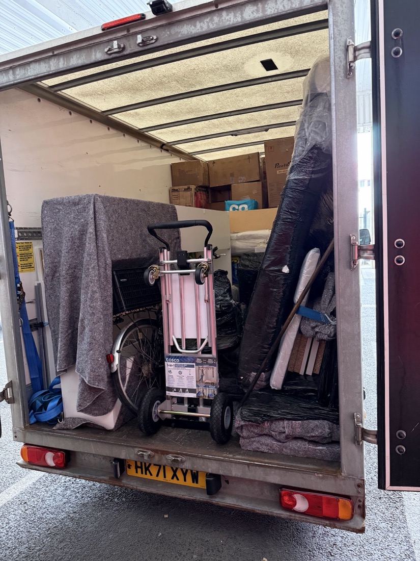 A fully loaded van with furniture wrapped in grey removal blankets and a folding trolley